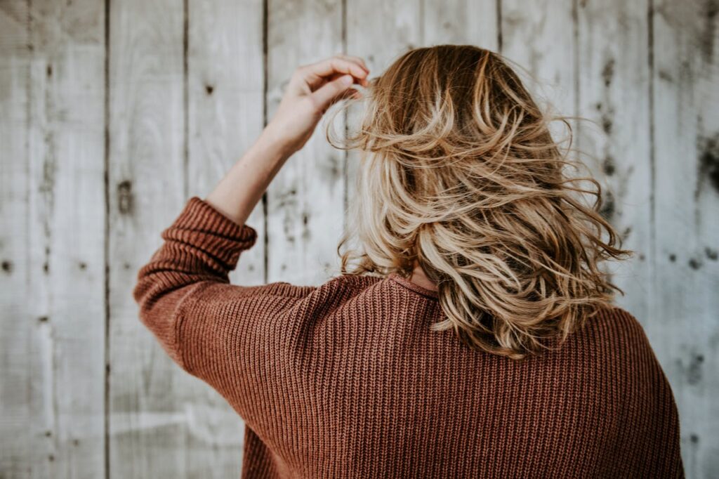 Rear view of a woman with blonde hair wearing a cozy sweater in front of rustic wooden wall.