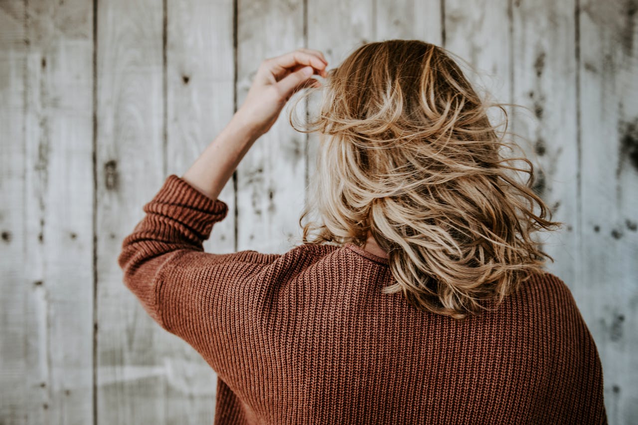 journey Rear view of a woman with blonde hair wearing a cozy sweater in front of rustic wooden wall.