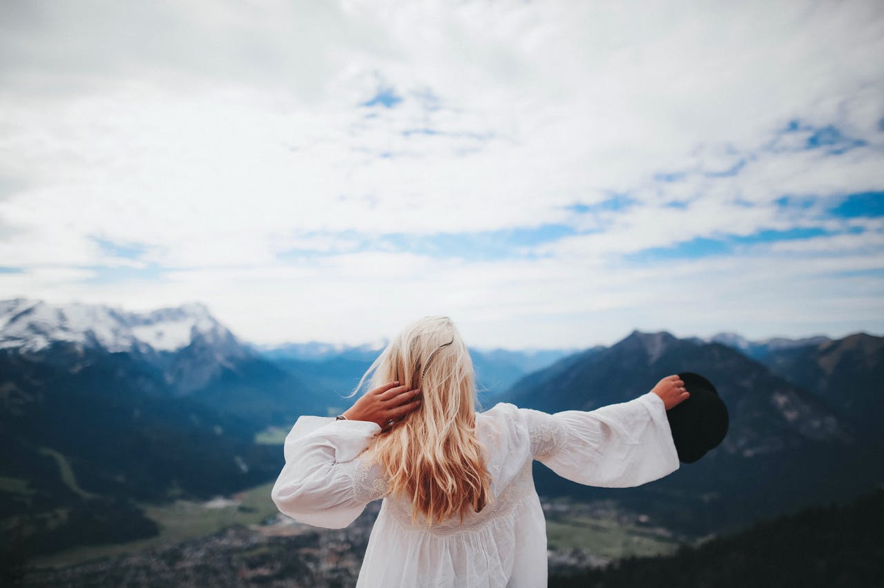services-04 Blonde woman in a white dress overlooks the beautiful mountain landscape of Ohlstadt, Germany.